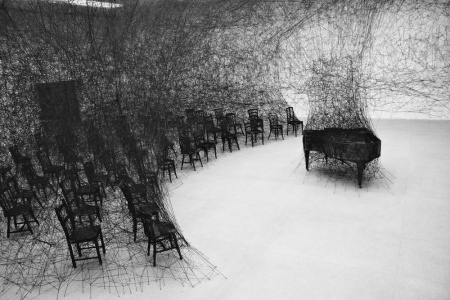 chiharu shiota - In silence installation When I first set my eyes on Japan-born, Berlin-based artist Chiharu Shiota's work, I wasn't sure if I was looking at an installation or a dark charcoal illustration. Though the piece echoes sketch-like imagery, it is in fact an installation piece involving a burnt piano in a room ravaged by black wool. The work known as In Silence is inspired by Shiota's own traumatic memories as a child, having witnessed her neighbor's house burn down. The charred piano is a direct memory of her neighbor's grand piano blazed up in smoke.  There is a melancholic aura that hovers throughout the incinerated room filled with singed furniture. The miles of thread woven in, around, and through each item within the space adds a feeling of entrapment. The way it engulfs the room's furnishings encapsulates the destructive and overwhelming nature of flames that have possessed one's material properties.
